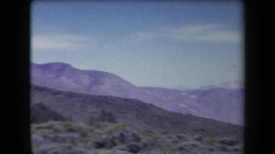1958 Arizona 8mm frame showing distant blue-purple mountains, scrub-covered slopes, and a pale sky with dark film borders.
