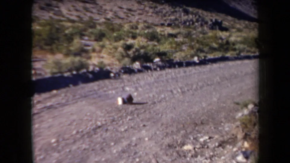 Late frame from the 1958 Arizona clip showing gravel roadside, sparse scrub, rocks, and two small indistinct objects.