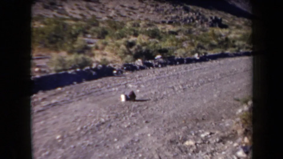 1958 Arizona home-movie frame showing a white can on a gravel road in a sparse desert landscape before the shot.