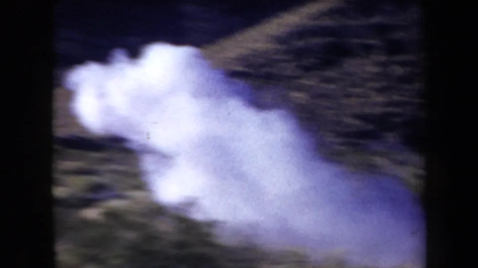 1958 Arizona home-movie frame showing a large smoke cloud after the shot, with desert terrain blurred behind it.