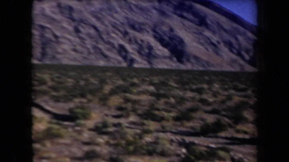 1958 Arizona frame ending on a blurred rocky desert slope and sparse vegetation after the shooting moment.