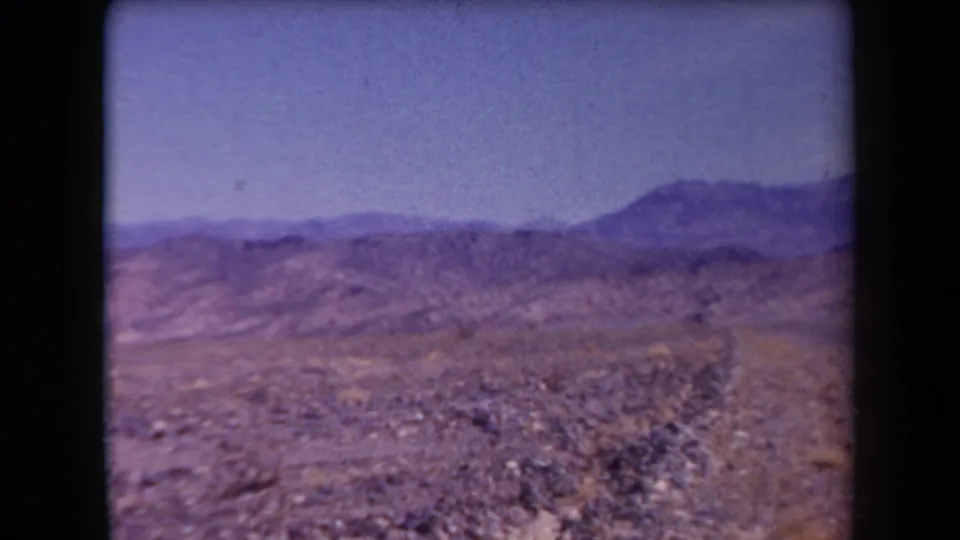 Wide 1958 Arizona home-movie view of open rocky desert, low ridges, and distant mountains under a pale blue sky.
