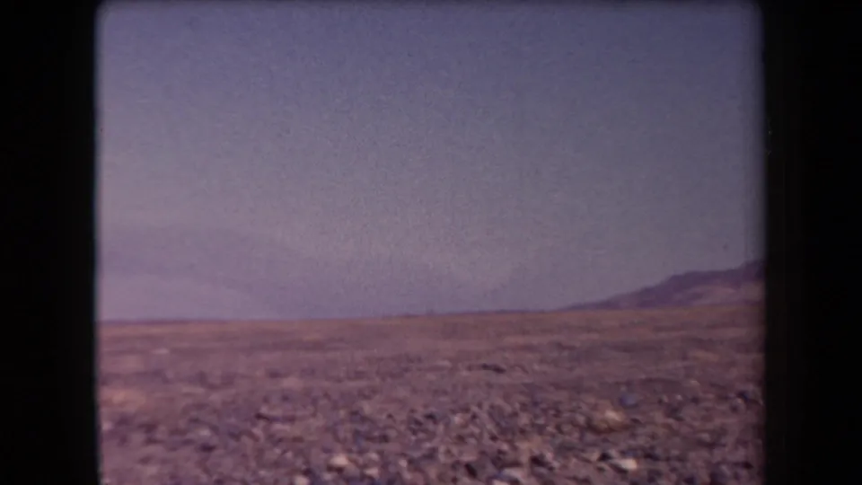 1958 Arizona 8mm frame showing a wide empty desert plain, low distant ridge, and hazy blue sky.