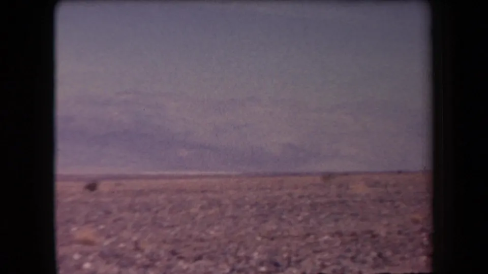 1958 Arizona 8mm frame showing a muted desert horizon, rocky foreground, and low mountains through soft haze.