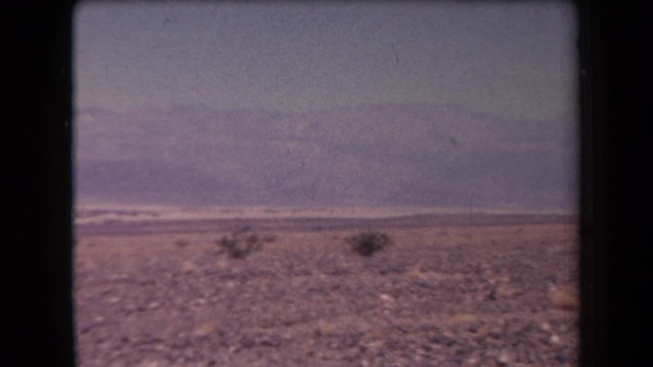 1958 Arizona home-movie frame of a broad rocky desert landscape with scattered low brush and distant mountain ridges.