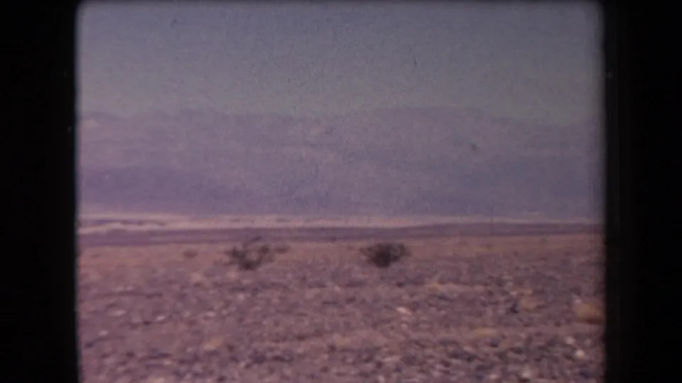 1958 Arizona home-movie frame of a broad rocky desert landscape with scattered low brush and distant mountain ridges.