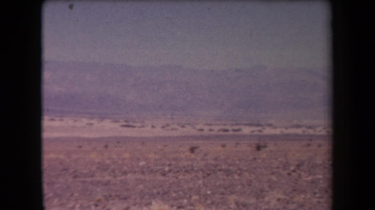 Wide desert plain with sparse scrub and distant low mountains under a hazy sky.