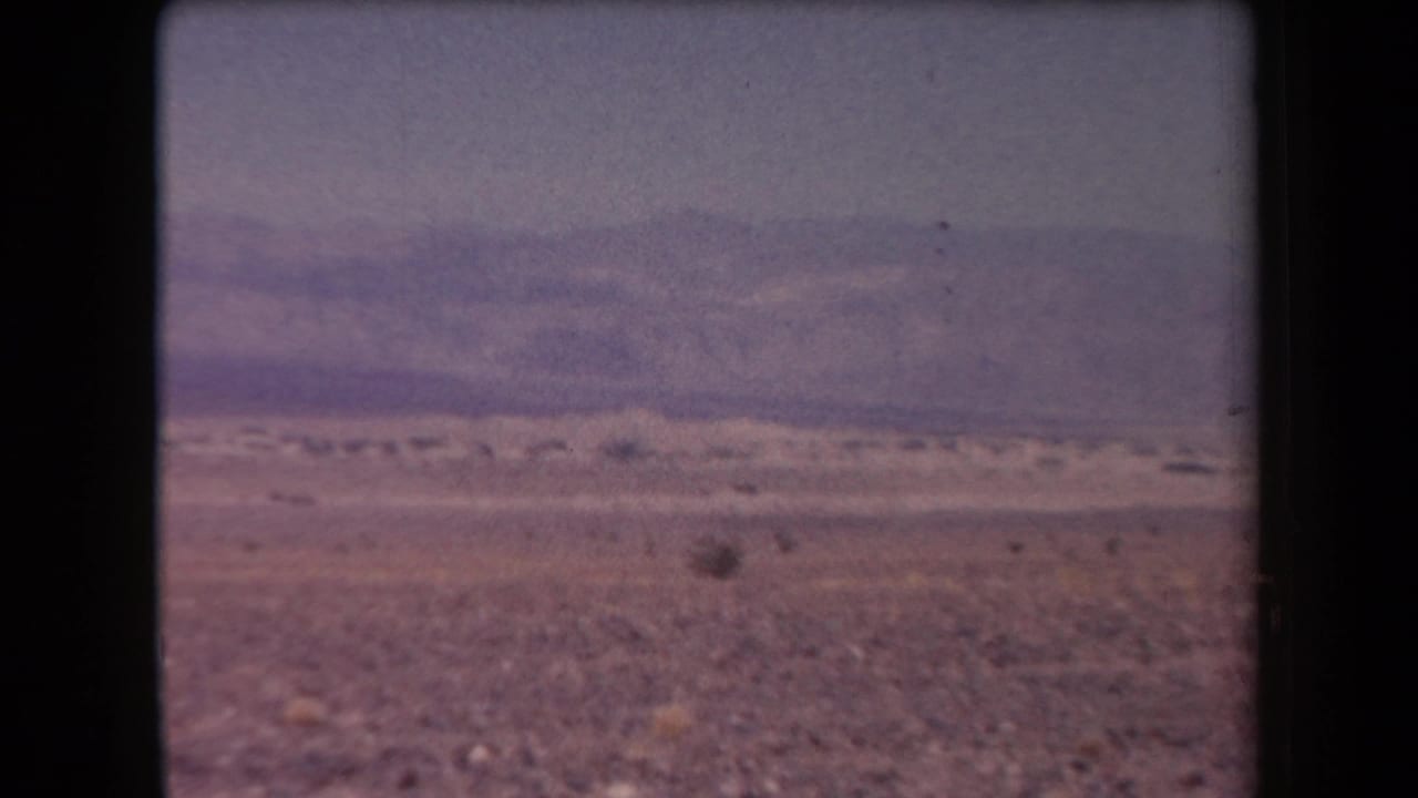 1958 Arizona desert view with scattered shrubs across a dry plain and distant mountains softened by haze.