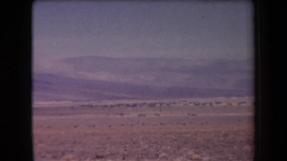 Arizona 8mm travel footage frame with rocky foreground, sparse vegetation, and a long hazy mountain range.