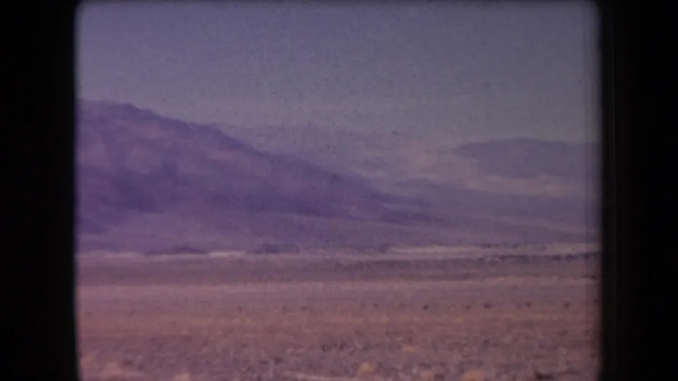 1958 Arizona frame showing an open desert plain and larger distant mountains, with faded color and soft 8mm focus.