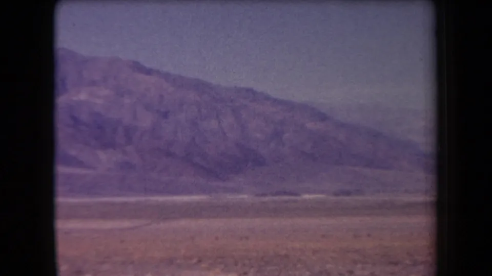 1958 Arizona 8mm frame showing a distant mountain range across an open desert plain with faded purple color and black reel borders.