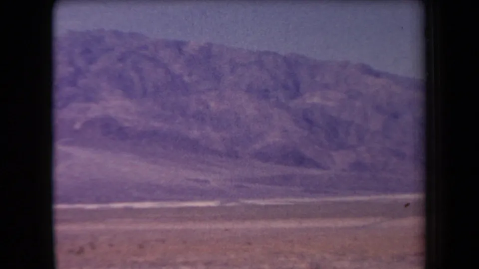 1958 Arizona home-movie frame of a rocky mountain range and dry valley floor, with soft focus and aged color shift.