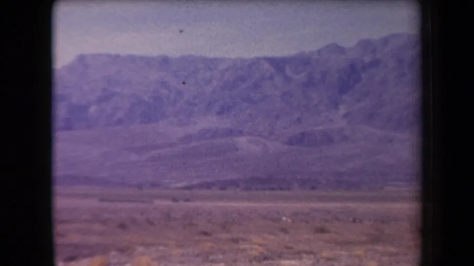 1958 Arizona home-movie frame showing low desert brush, a broad plain, and purple-toned mountains in the distance.