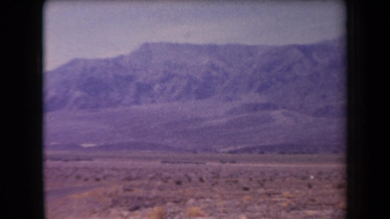1958 Arizona home-movie frame showing a broad desert plain with low scrub and a distant mountain ridge under a pale sky.