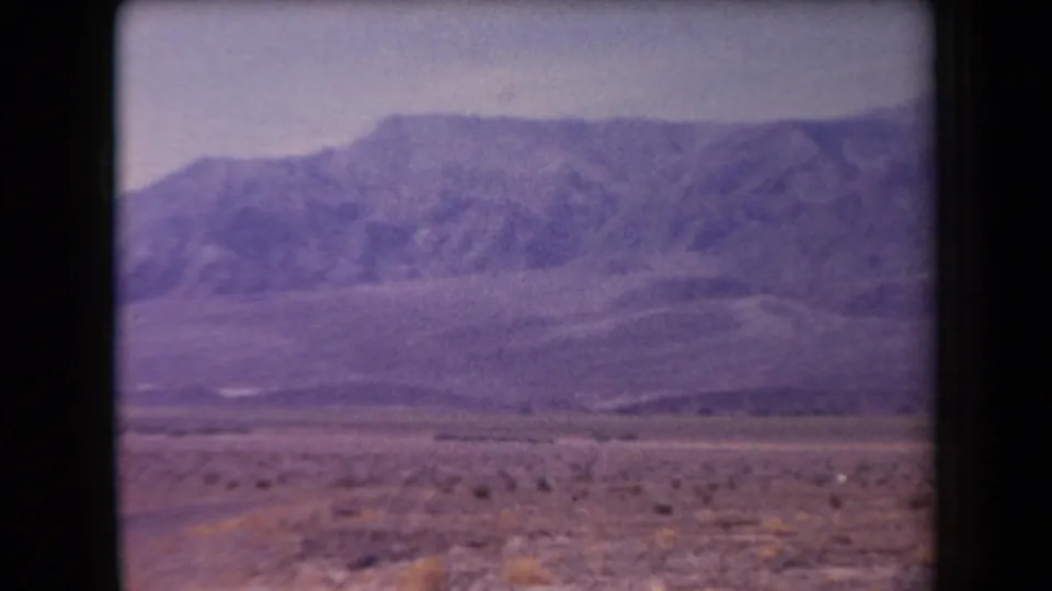 1958 Arizona home-movie frame showing a broad desert plain with low scrub and a distant mountain ridge under a pale sky.