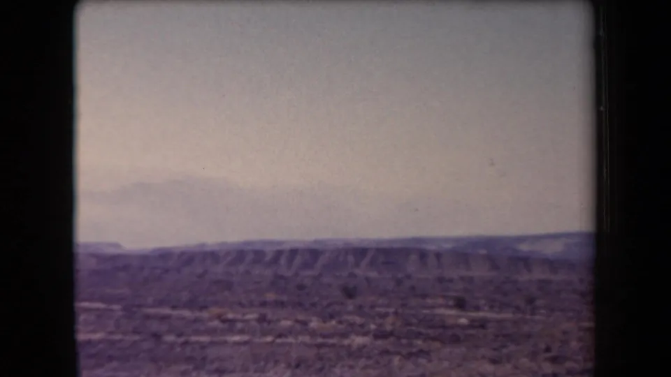 1958 Arizona travel footage frame with arid foreground, layered desert ridges, and faint mountains in haze.