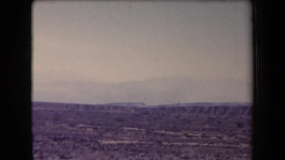 1958 Arizona 8mm frame showing low desert hills, rough arid ground, and a broad pale sky.