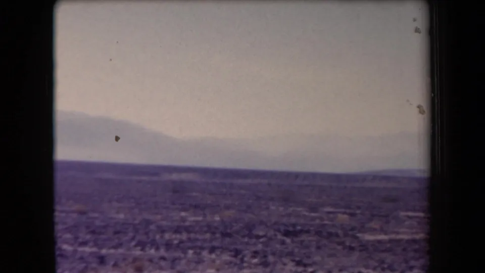 1958 Arizona home-movie frame with a broad desert horizon and faint mountain silhouette in haze.