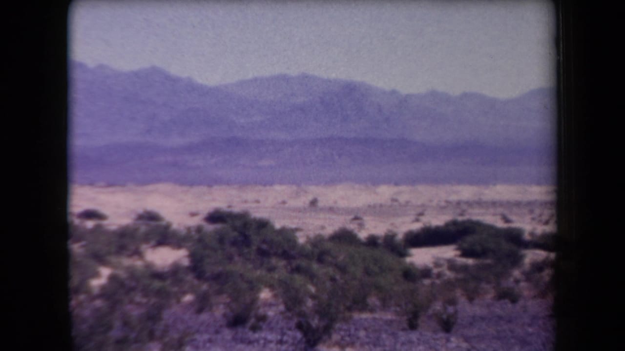 Desert shrubs in the foreground with mountain ridges beyond.