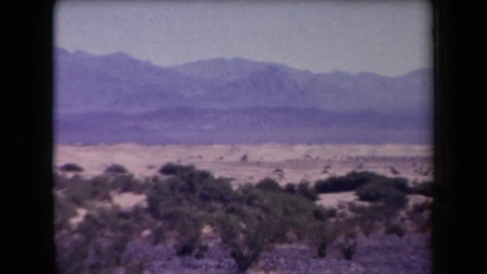 1958 Arizona desert view with scrubby vegetation in the foreground and layered mountain ridges in the distance.