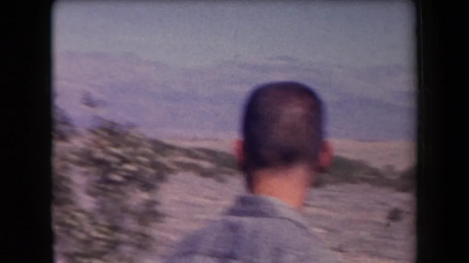 1958 Arizona home-movie frame showing an adult man from behind as he looks toward a sandy desert slope and hazy mountain backdrop.