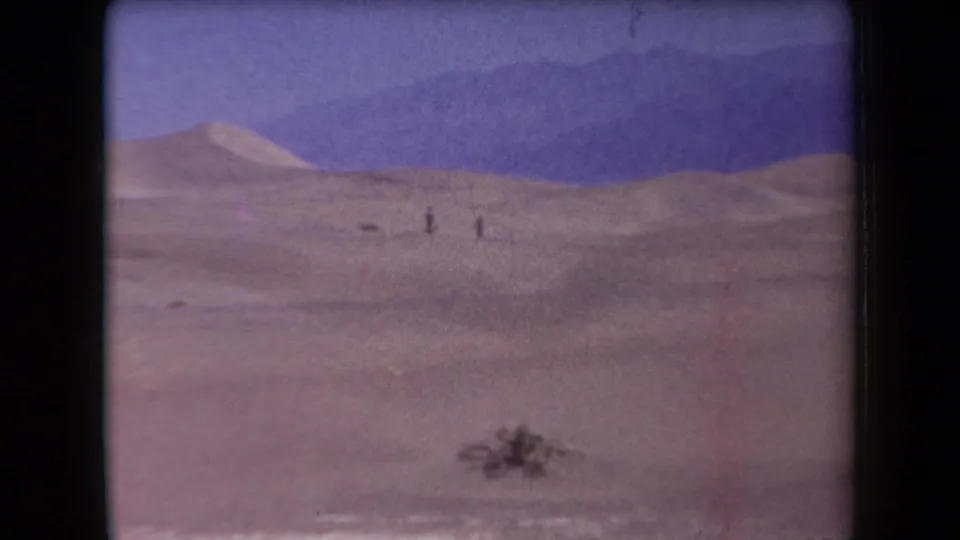 1958 Arizona desert view with distant walkers crossing open dunes beneath a purple-blue sky.