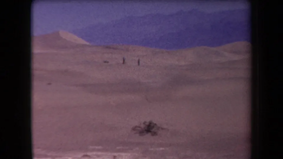 Final 1958 Arizona desert frame with small human figures on rolling dunes and mountains behind them.