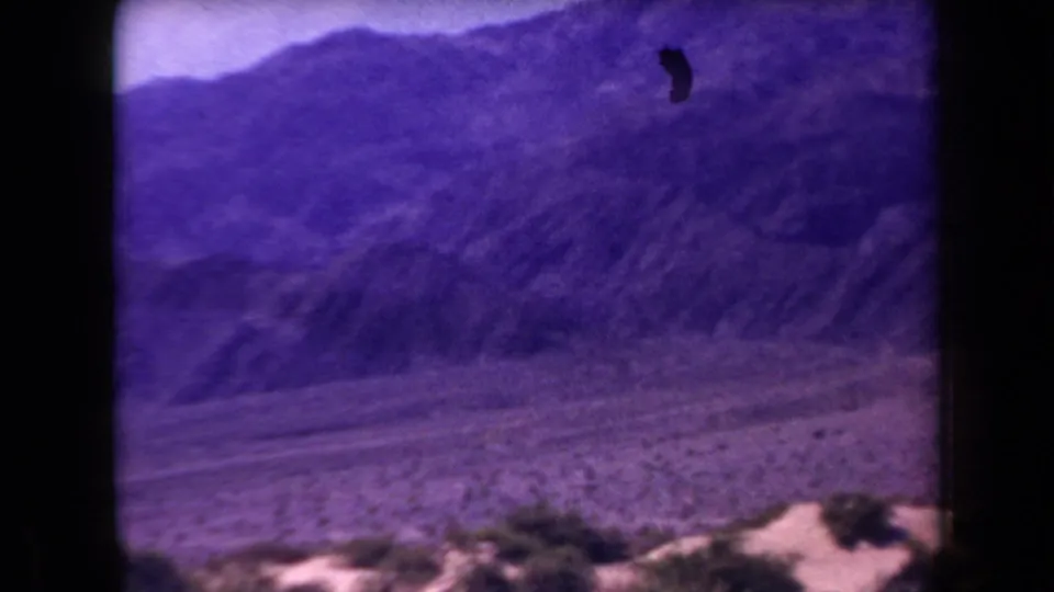 1958 Arizona 8mm frame showing a desert valley below layered mountains, with visible film speckling and strong purple color shift.