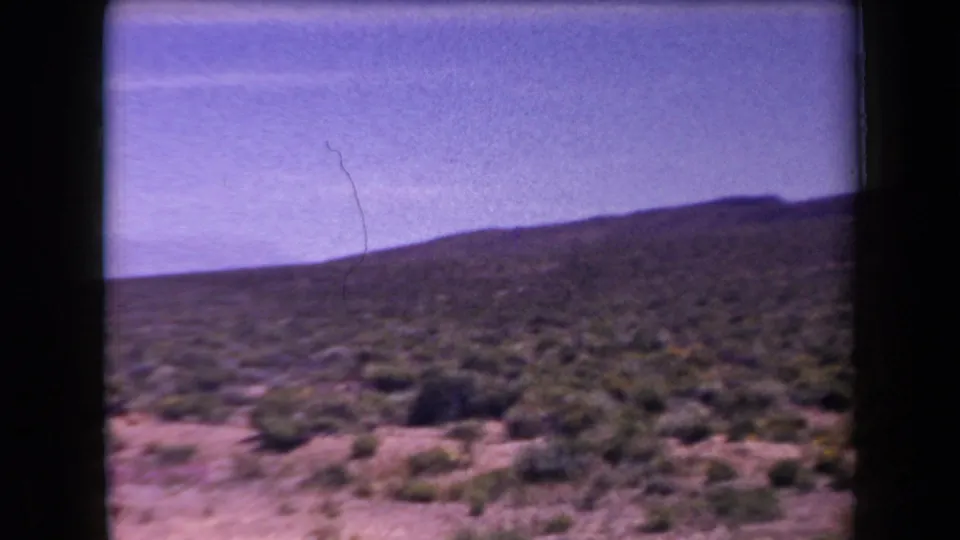 1958 Arizona desert landscape with scattered shrubs, a distant ridge, open sky, and visible 8mm grain and color shift.