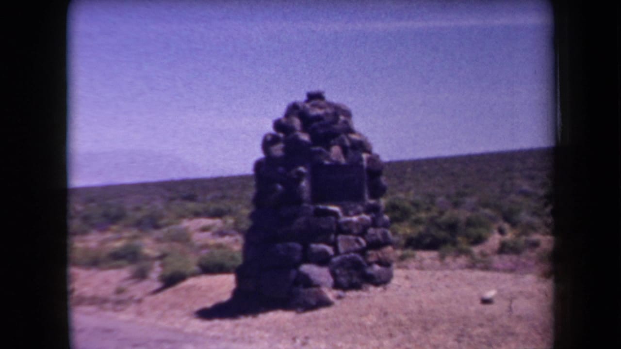 Small stone monument standing in scrub desert beside a roadside area.