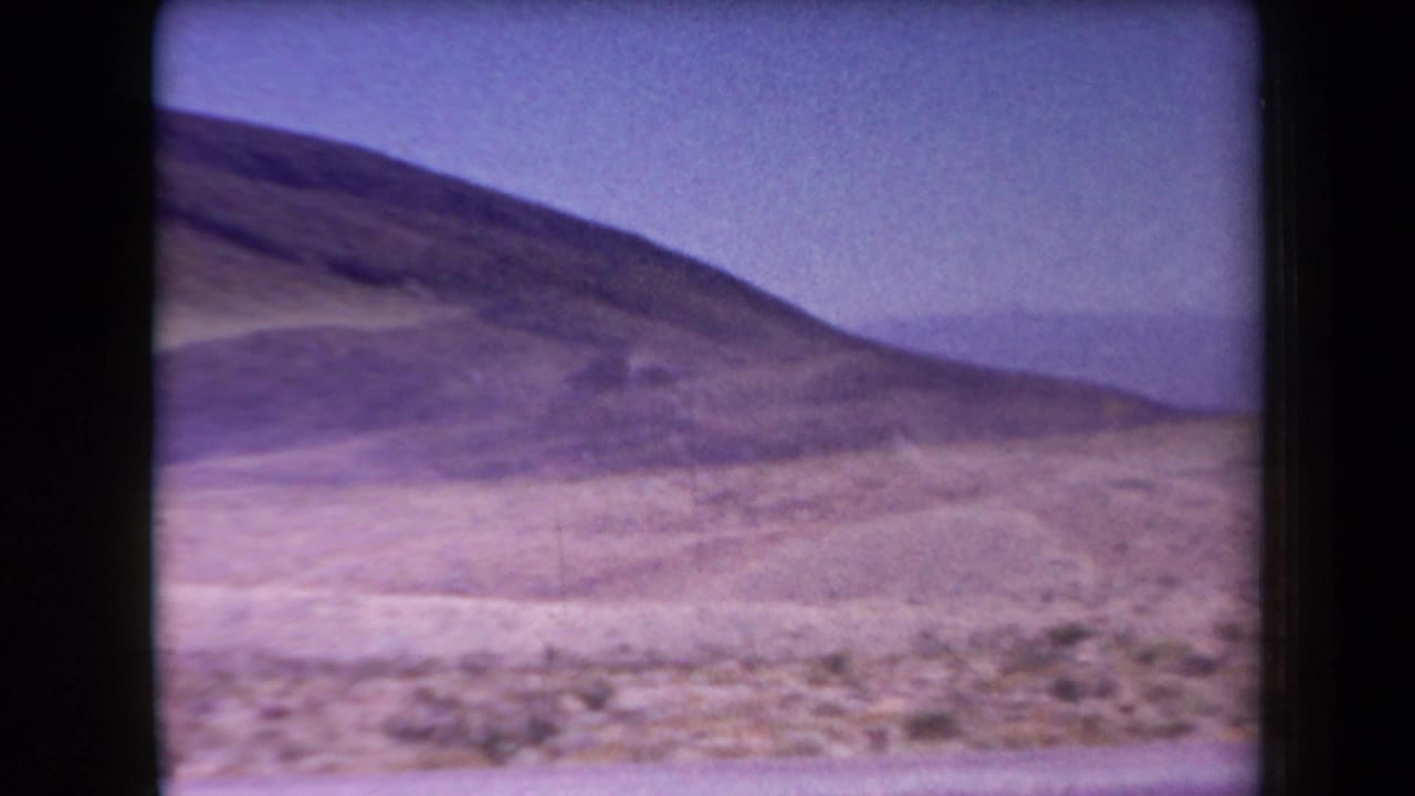 Dry hillside and open desert terrain seen through a soft, purple-tinted film frame.