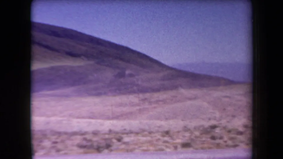 Arizona desert landscape from the 1958 8mm clip, with a low hillside, pale ground, sparse vegetation, and hazy sky.