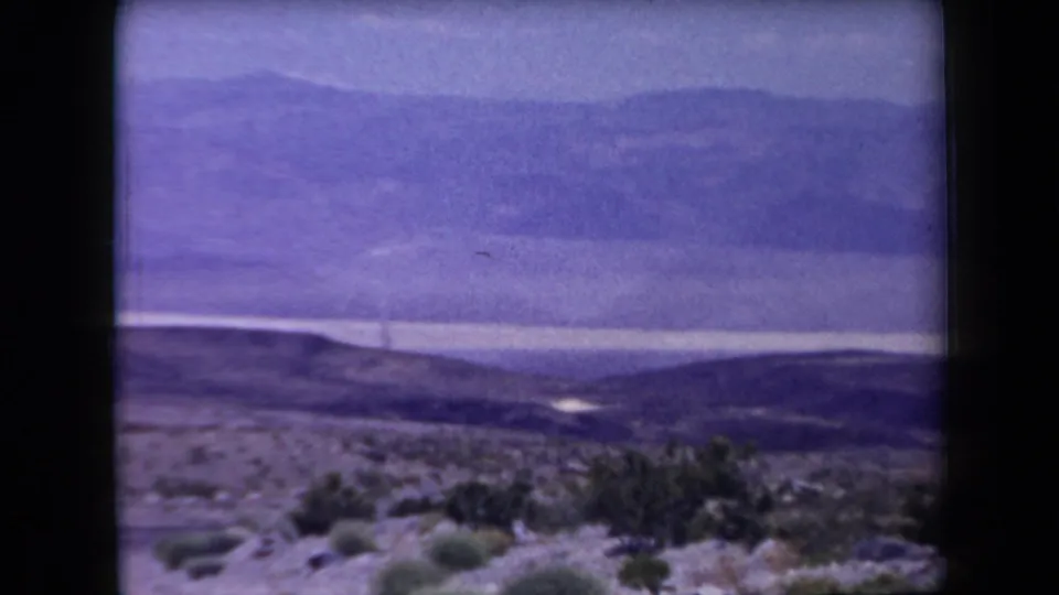 1958 Arizona landscape frame showing low desert vegetation, rolling terrain, distant mountains, and visible 8mm frame borders.