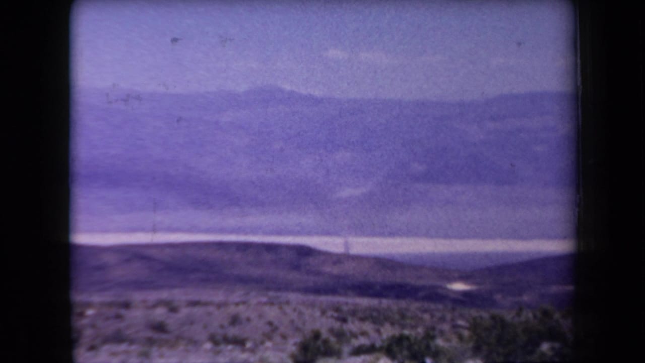 1958 Arizona desert panorama with scattered shrubs in the foreground, low hills, distant mountains, and soft 8mm color shift.