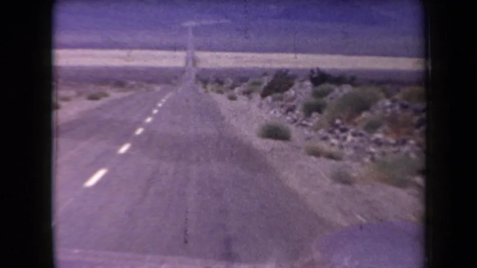 1958 Arizona 8mm forward-driving view of an empty highway through rocky desert terrain with scattered shrubs and distant hills.