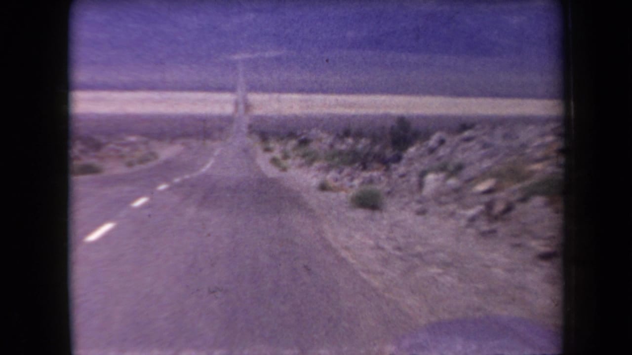 Straight desert highway receding toward the horizon with rocky ground on both sides.