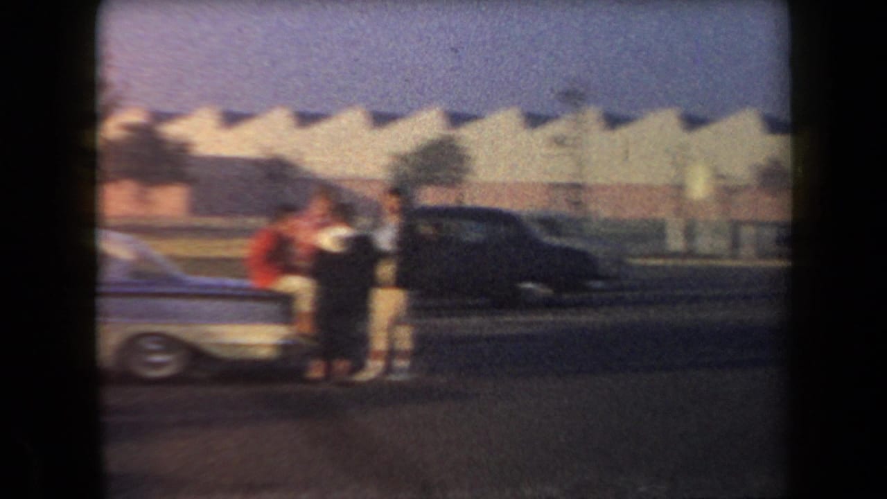 1958 Arizona home-movie frame showing several people near parked mid-century cars along a roadside.