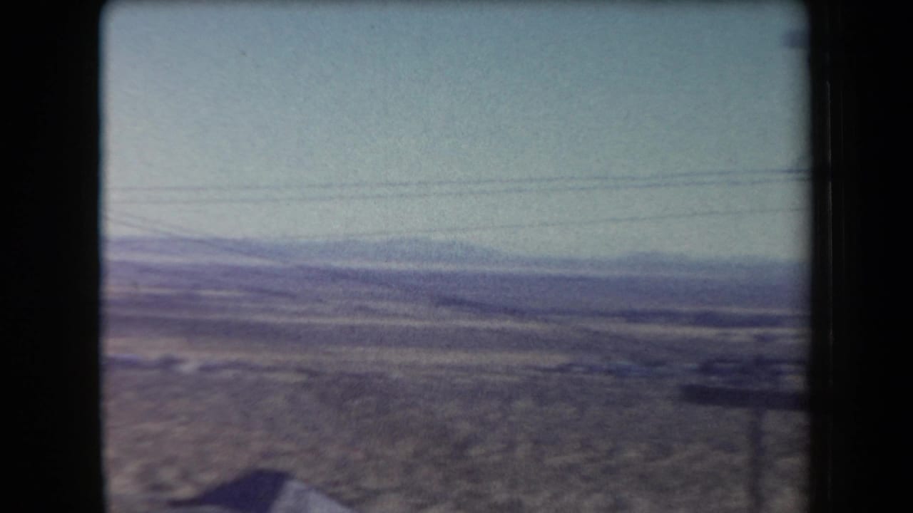 Wide desert valley with low mountains, utility wires, and a dark structure at the edge of frame.