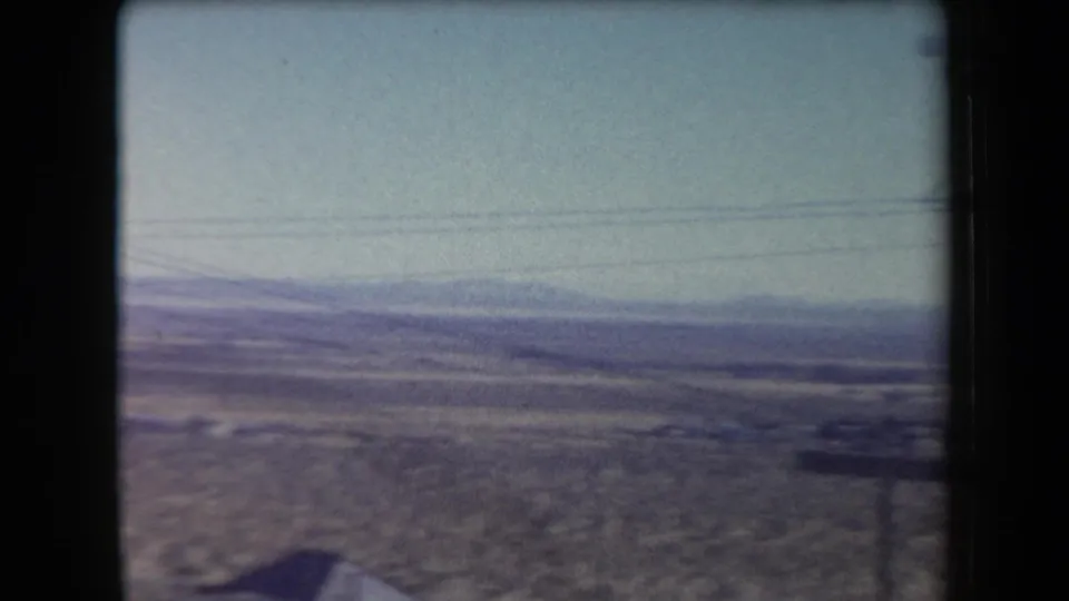 1958 Arizona 8mm frame looking across open desert flats toward low mountains, crossed by overhead utility wires.