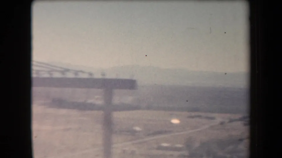1958 Arizona 8mm frame with a utility pole crossarm, pale desert road, scrubland, and faint mountains in haze.