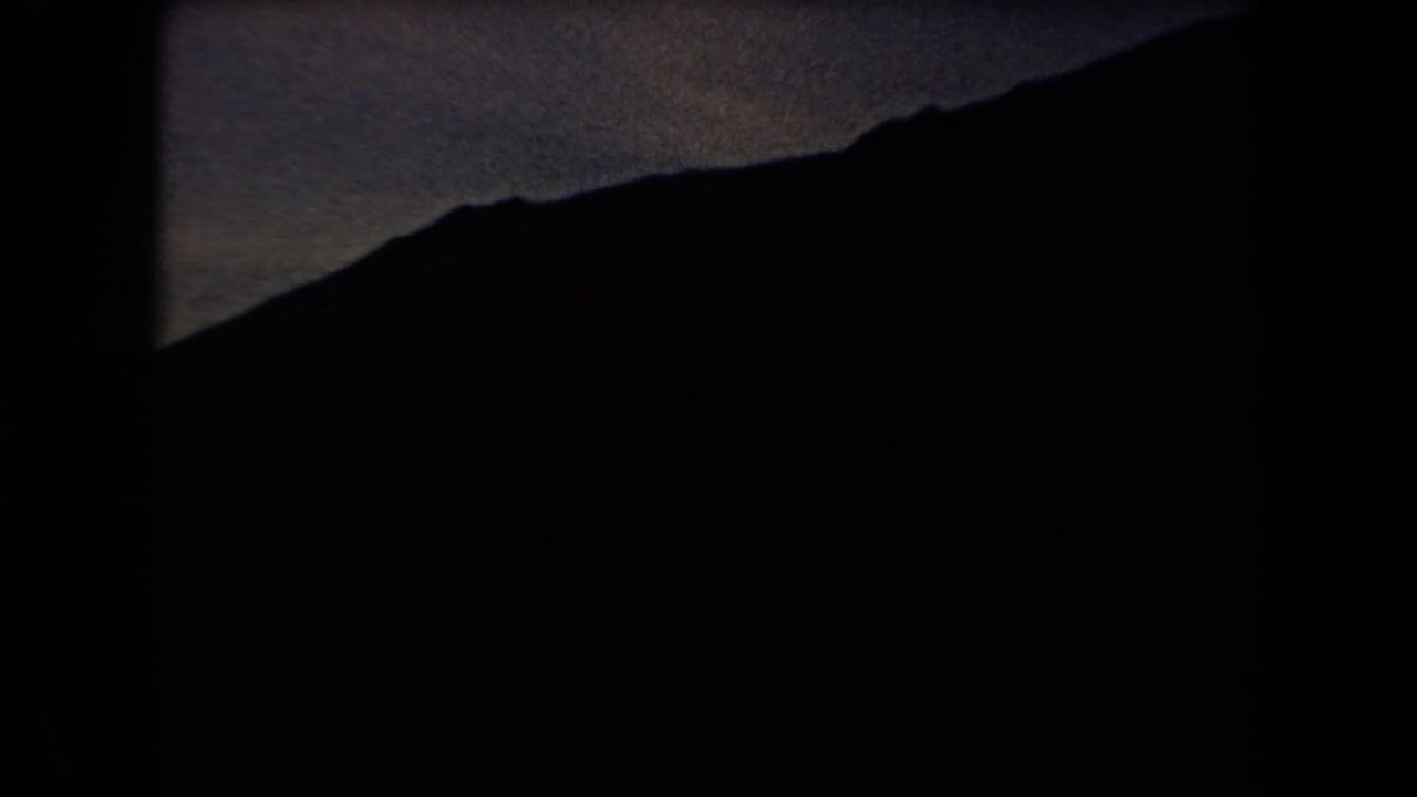 Dark mountain ridge above a dim valley under a fading sky.