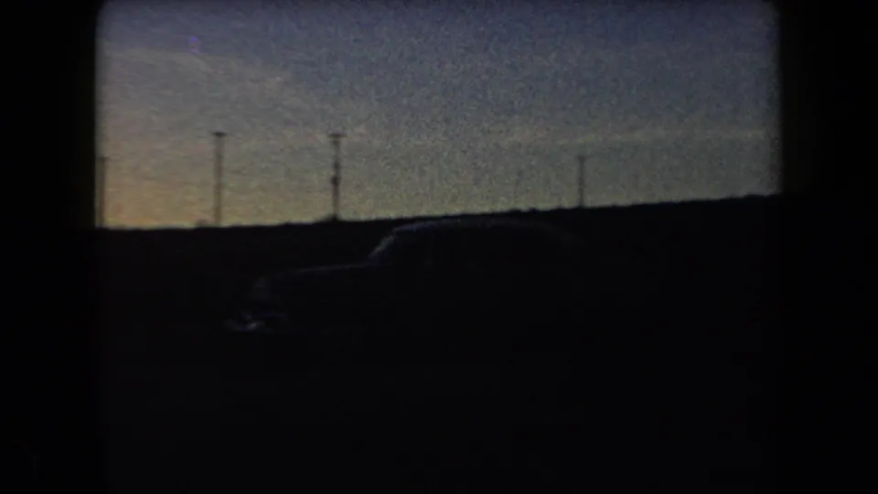 Arizona 1958 roadside overlook with a dark parked car silhouette, utility poles, and distant hills at dusk.