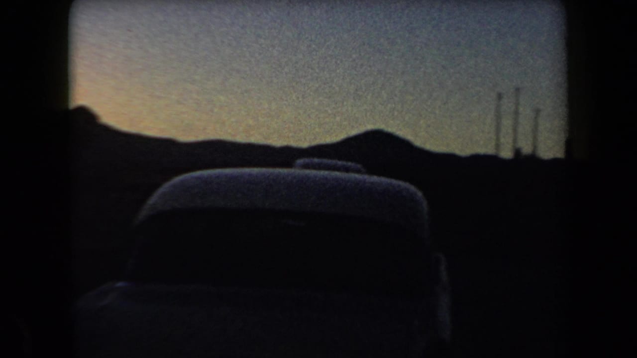 1958 Arizona 8mm frame showing silhouetted parked cars, low hills, and faint smokestack shapes under a dim sunset sky.