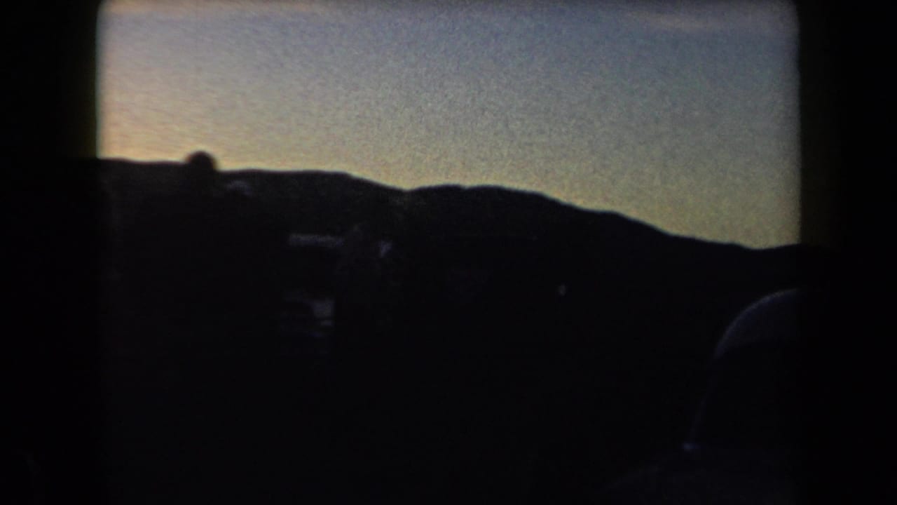 Low hill horizon and dark vehicle shapes seen through a dim frame.