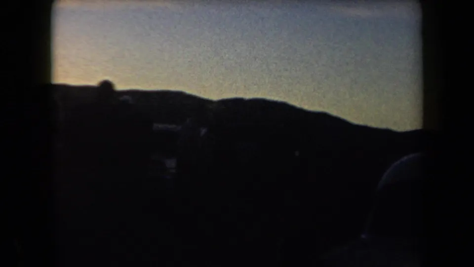 1958 Arizona road-view frame with dark vehicle silhouettes below a low hill horizon and fading evening light.