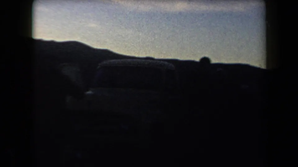 1958 Arizona 8mm frame with dark car silhouettes, a low ridge line, and a soft dusk sky recorded from a home-movie viewpoint.