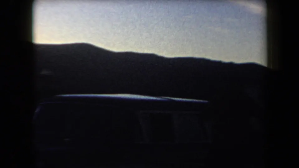 1958 Arizona 8mm frame showing a dark car front or side detail below a silhouetted hill line at dusk.