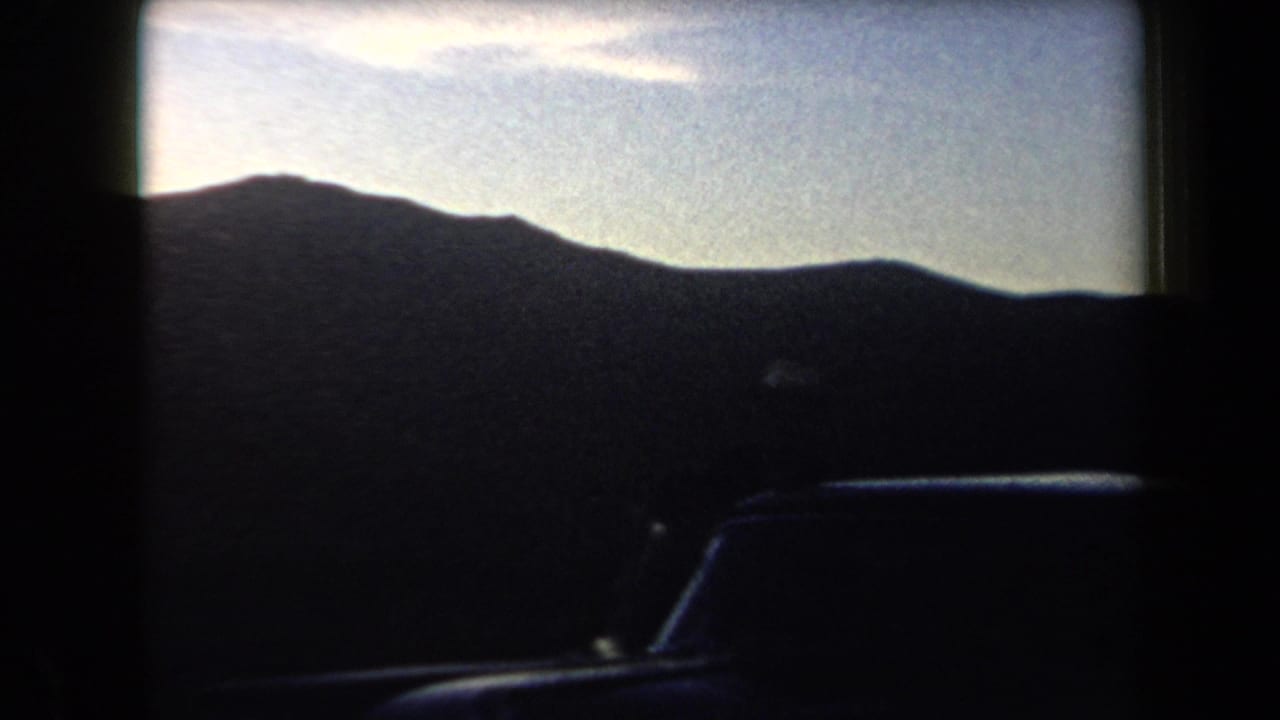 1958 Arizona home-movie frame showing a silhouetted mountain ridge under a pale sky, partly framed by dark window or film edges.