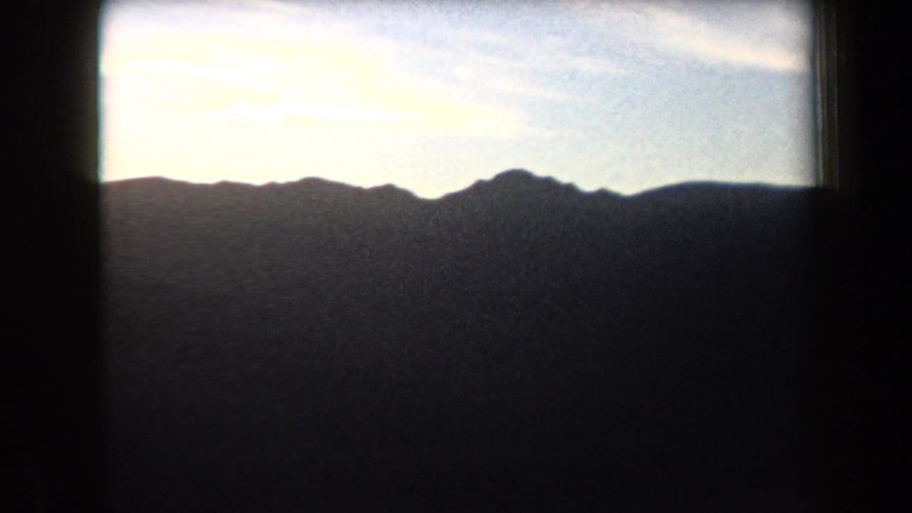 Jagged dark mountain peaks stretch across the horizon below a bright sky.