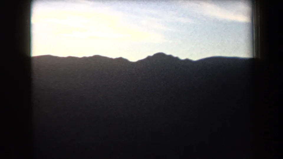 1958 Arizona frame with jagged mountain silhouettes across the horizon and a bright, softly clouded sky above.